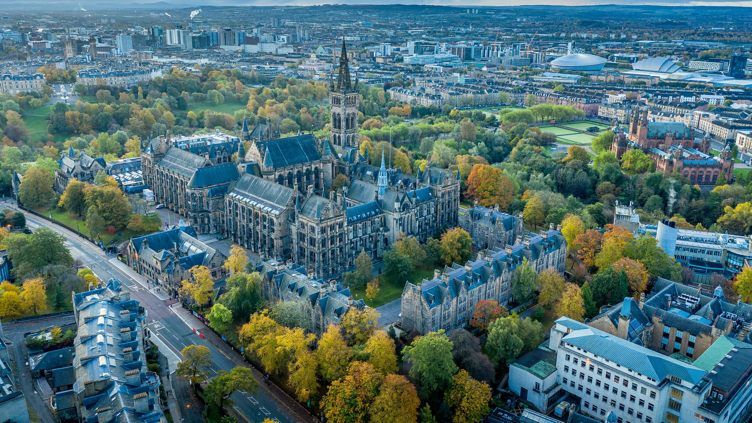 An aerial view of the University of Glasgow among autumn trees, with the city beyond