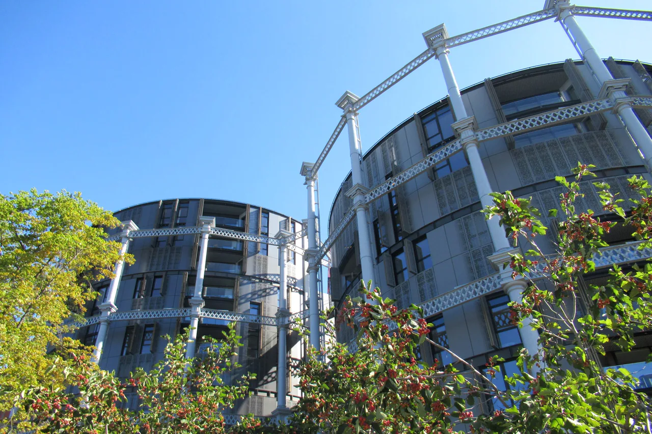 Round blocks of flats built inside the restored iron frames of the old gas holders at King's Cross, behind trees with red berries