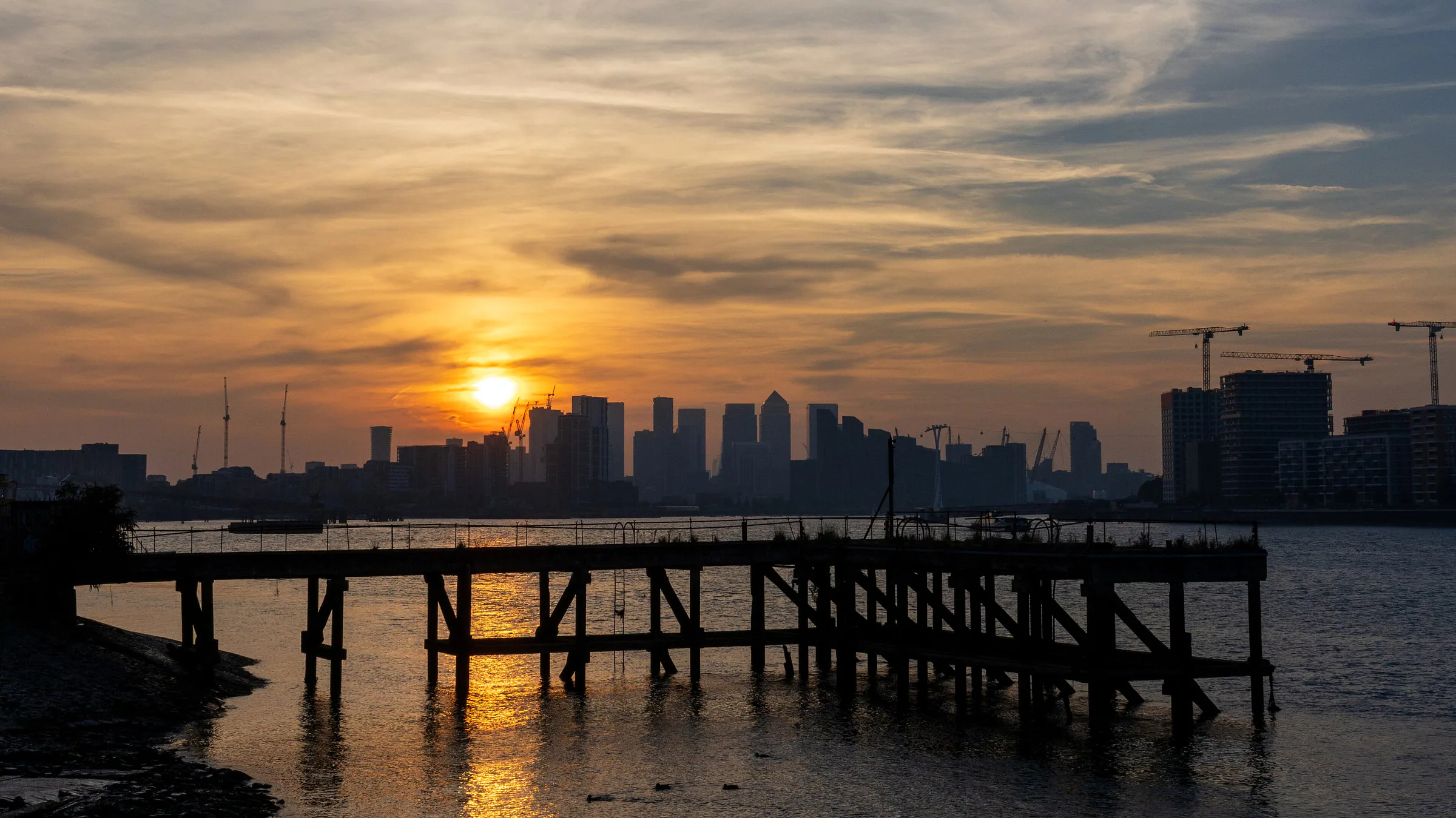 The sun setting behind the Canary Wharf towers, seen along the Thames from the Barrier