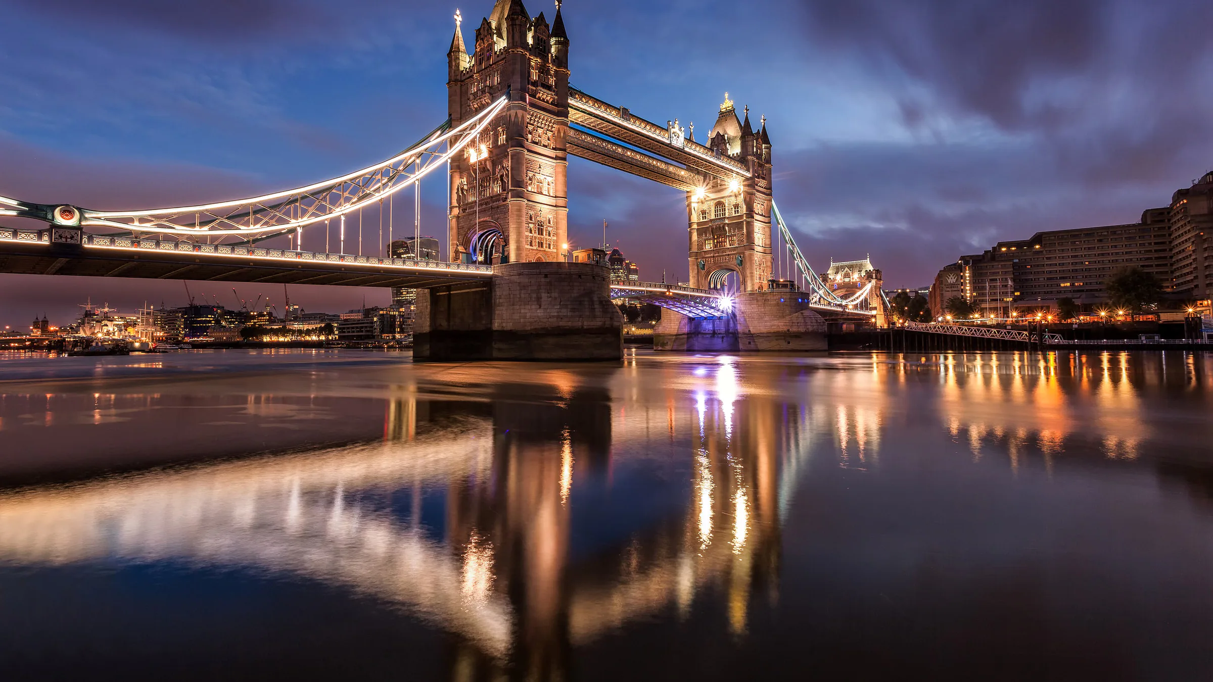 Tower Bridge lit before sunrise, with the river still and dark