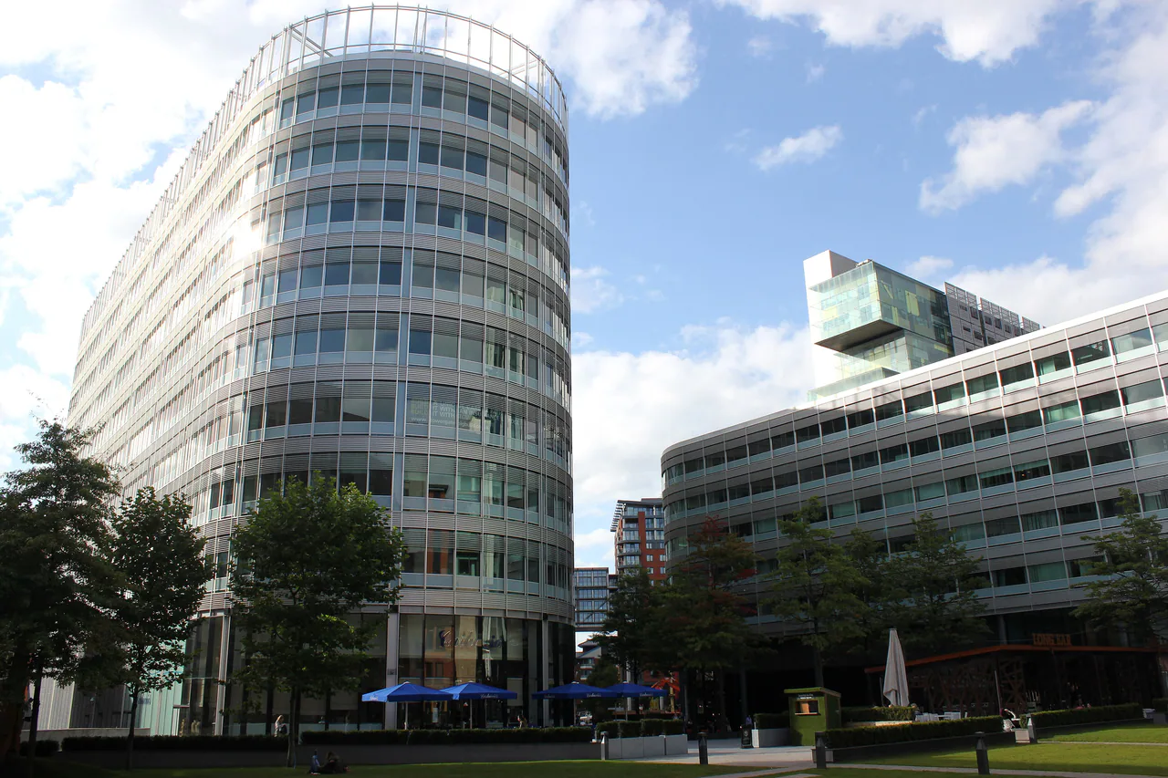 Curved glass office buildings around the lawn of Hardman Square in Spinningfields, Manchester, with blue parasols on the square