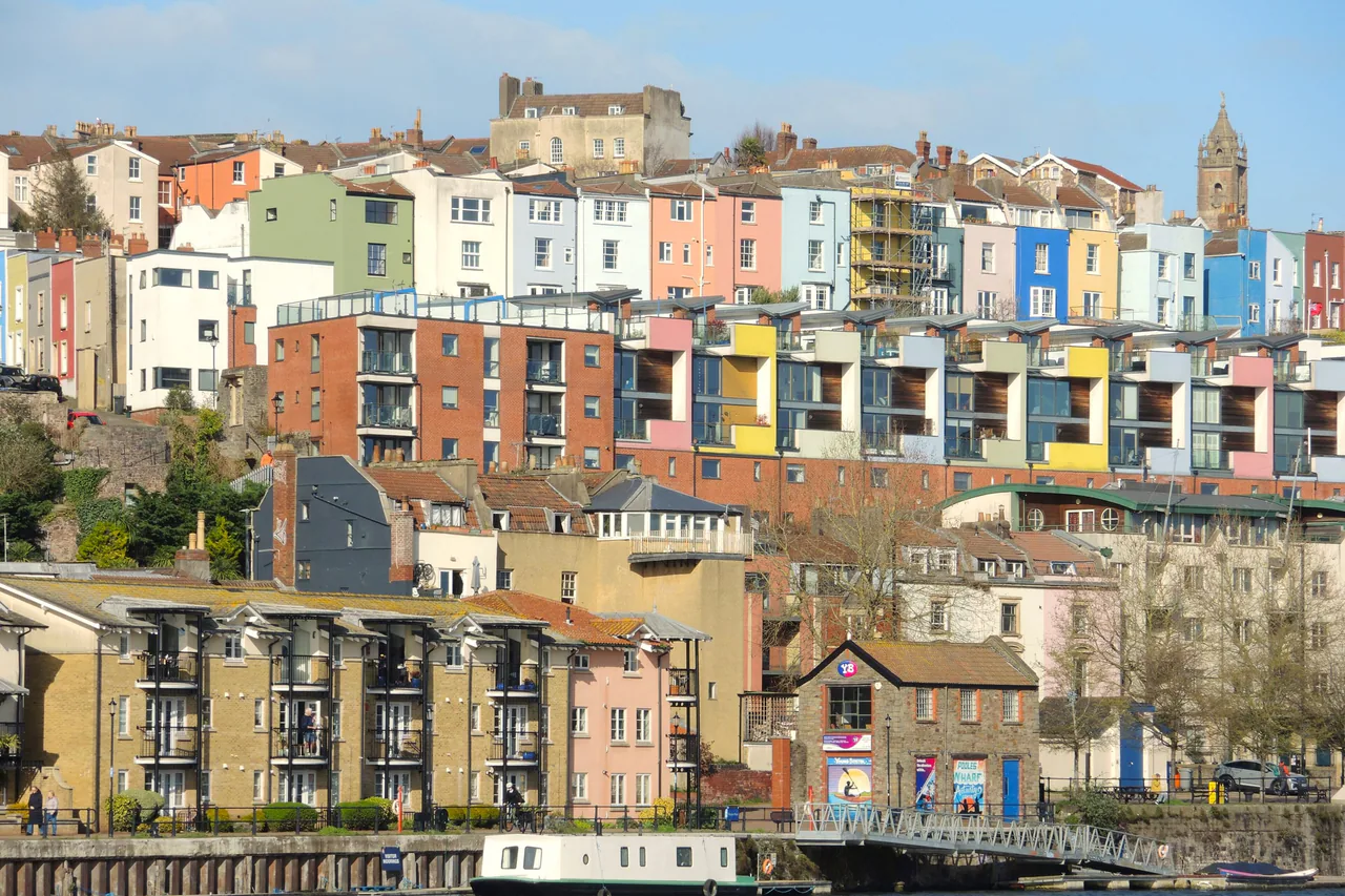 Rows of brightly painted houses and flats climbing the hill above Bristol's harbour, with Cabot Tower on the skyline
