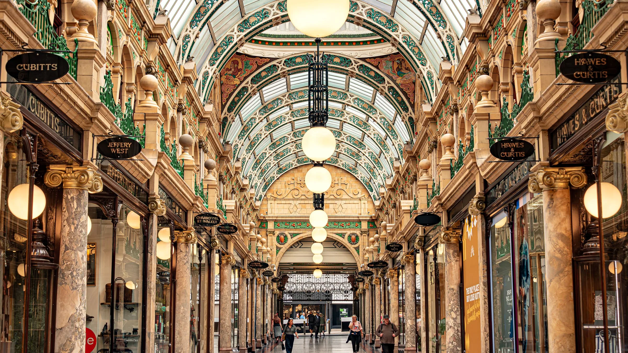A shopping arcade in the Victoria Quarter, Leeds, with marble columns, round hanging lamps and a painted glass roof