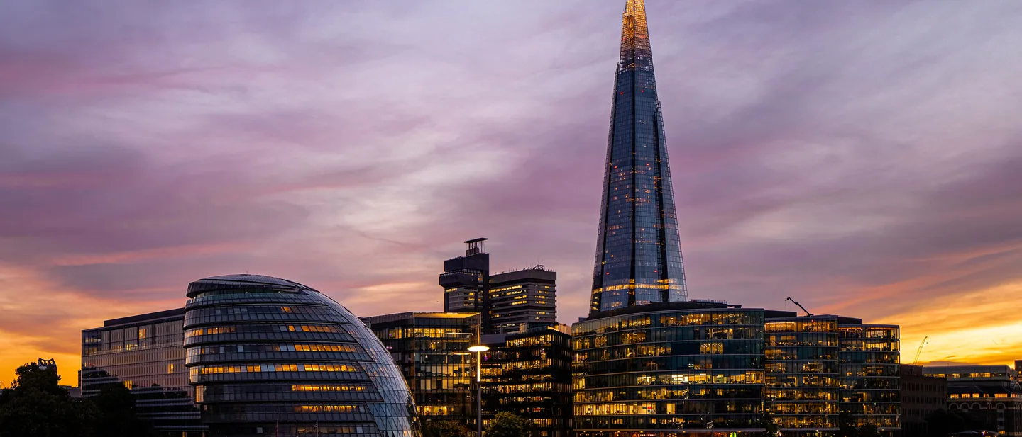 The Shard and the rounded glass former City Hall lit up against a pink and orange sunset, their lights reflected in the Thames