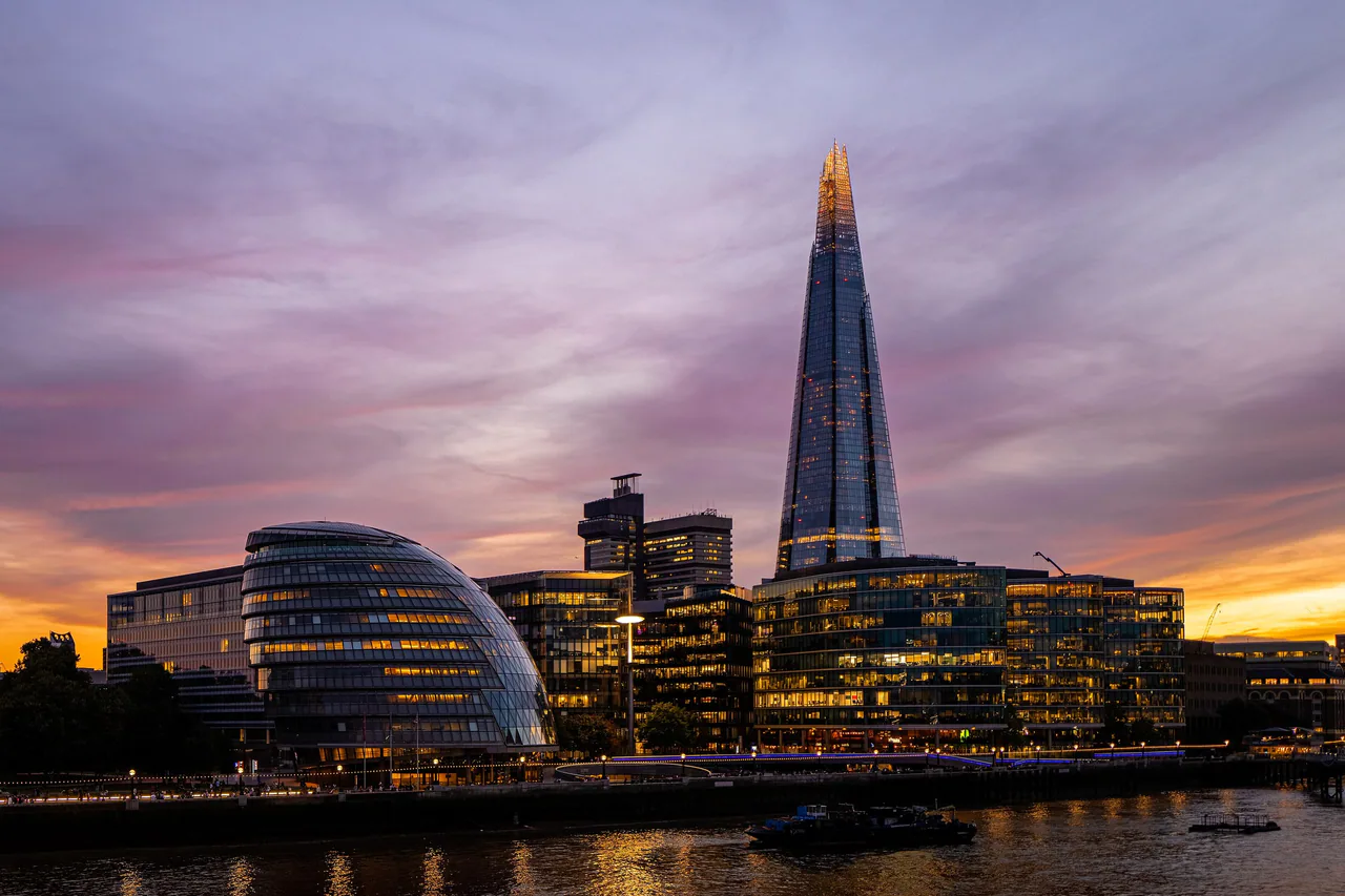 The Shard and the rounded glass former City Hall lit up against a pink and orange sunset, their lights reflected in the Thames