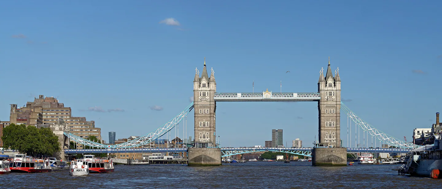 Tower Bridge under a clear blue sky, seen from the Thames, with tour boats moored along both banks