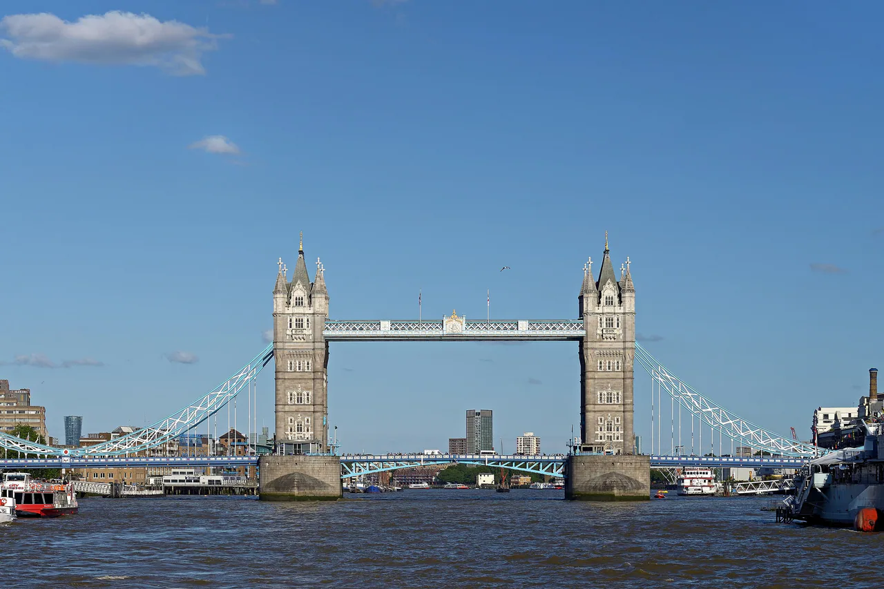 Tower Bridge under a clear blue sky, seen from the Thames, with tour boats moored along both banks