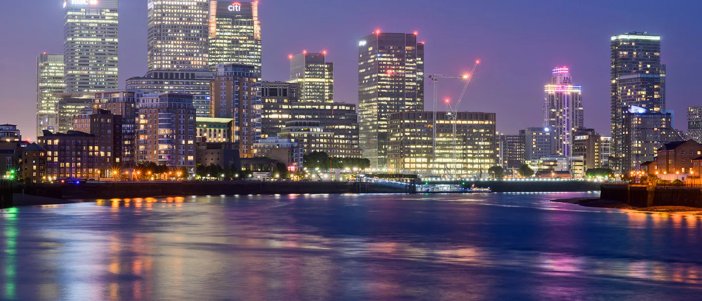 The towers of Canary Wharf lit against a deep blue evening sky, seen from Limehouse