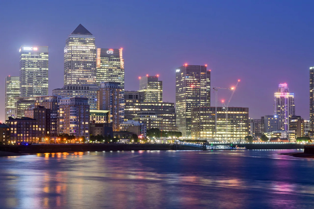 The towers of Canary Wharf lit against a deep blue evening sky, seen from Limehouse