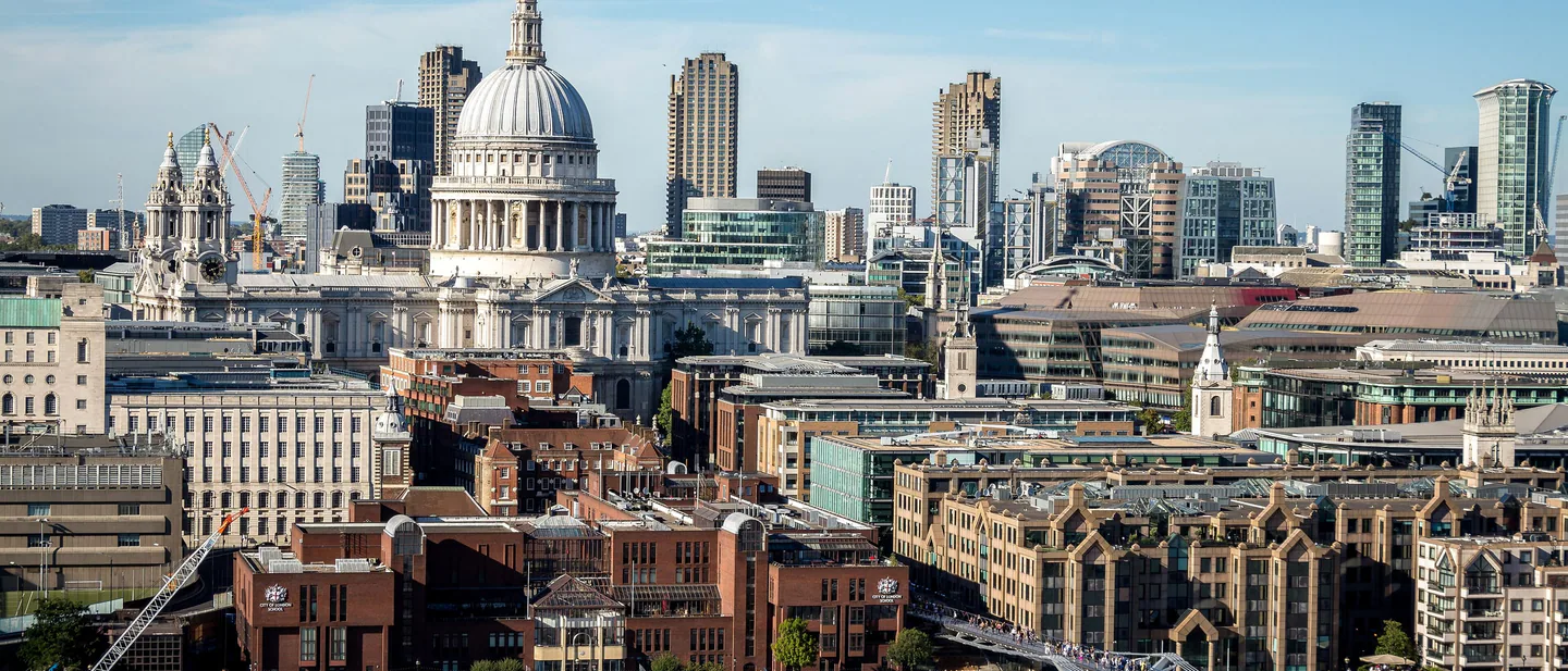 The dome of St Paul's Cathedral above the north bank of the Thames, with people crossing the Millennium Bridge and City towers behind