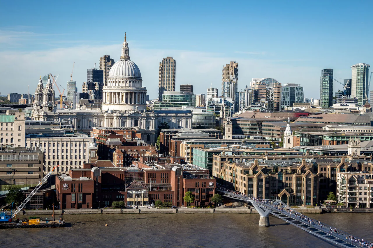 The dome of St Paul's Cathedral above the north bank of the Thames, with people crossing the Millennium Bridge and City towers behind