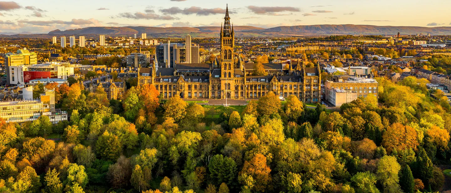 The University of Glasgow tower rising above autumn trees in Kelvingrove Park at sunrise