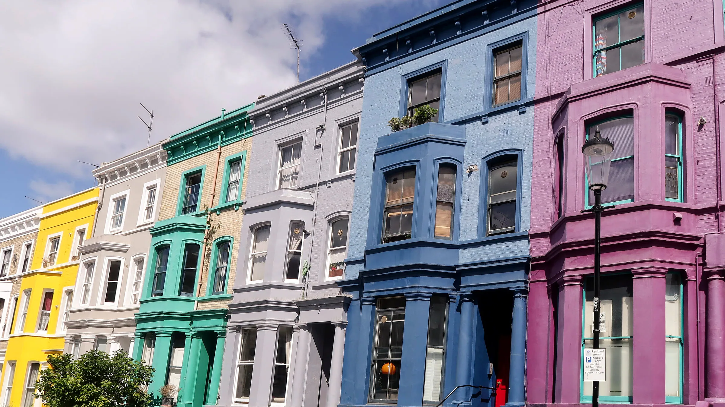 A row of tall terraced houses painted yellow, green, grey, blue and purple on Lancaster Road in Notting Hill, west London